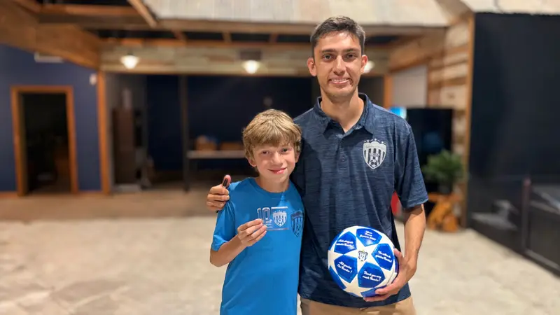 A young player holding a signed ball next to an older Juniors player