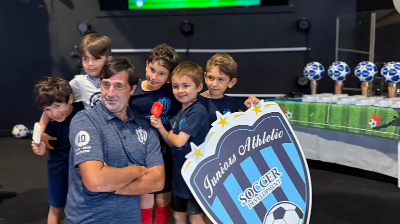 A coach and two young players with popsicles next to the Juniors crest